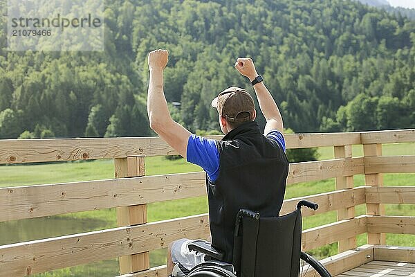 Behinderter junger Mann im Rollstuhl in der Natur  aufgeregt und voller Optimismus wie ein Gewinner