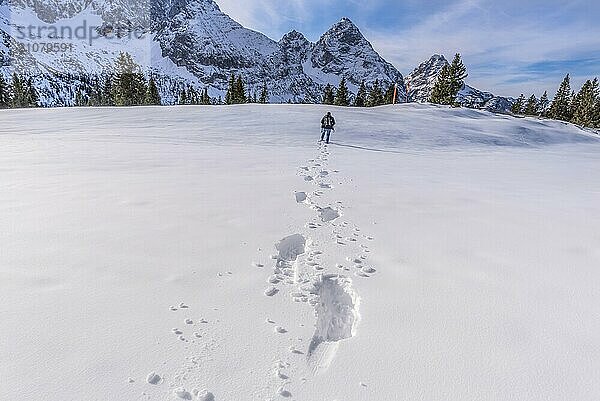 Winterlandschaft mit einem Mann  der auf einem Berggipfel durch den Schnee geht und eine Spur von Fußspuren hinter sich lässt. Bild aufgenommen in den österreichischen Alpen  in der Nähe des Ferienortes Ehrwald