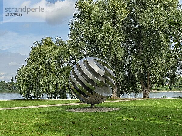 Eine moderne Skulptur aus Metall in Form einer Kugel steht in einem grünen Park nahe einem Fluss  bonn  rhein  deutschland