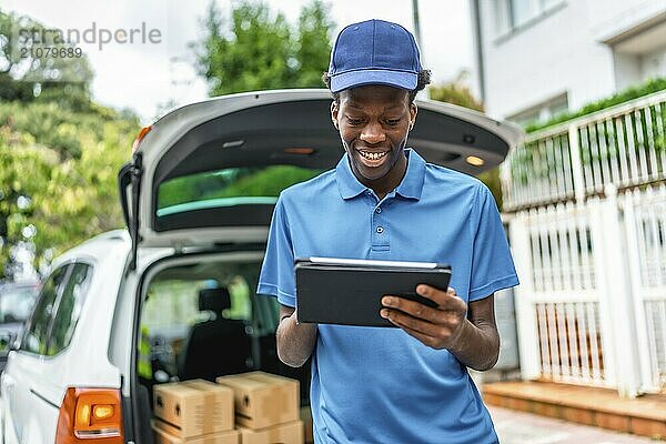 Fröhlicher afrikanischer Mann  der mit einem Tablet arbeitet  während er mit einem Lieferwagen Pakete ausliefert