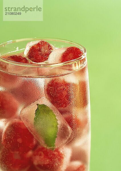 Gefrorene Himbeeren und Minzblatt in einem Glas Wasser auf grünem Hintergrund. Glas Wasser mit Hintergrundbeleuchtung