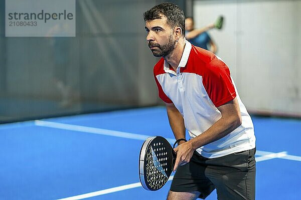 Seitenansicht eines reifen  sportlichen Mannes  der in einer Halle Paddle Tennis spielt