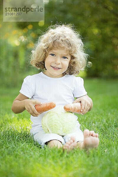 Glückliches Kind spielt mit Gemüse auf grünem Gras im Freien im Frühling Park