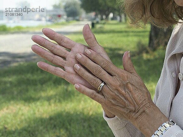 Ältere Frau massiert ihre Hände mit Feuchtigkeitscreme und pflegt ihre alternde Haut in einer friedlichen Umgebung im Freien