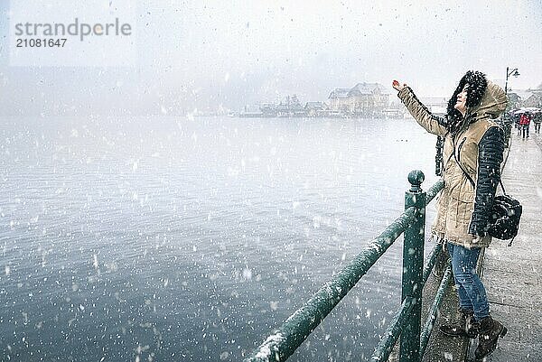 Glückliche junge Frau  die den ersten Schneefall genießt und die Schneeflocken auffängt  am Ufer des Hallstatter Sees in der Gemeinde Hallstatt in Österreich