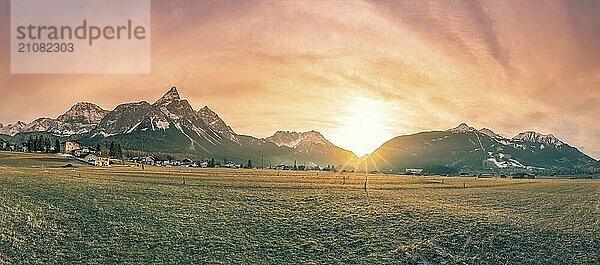 Alpenpanorama mit den österreichischen Alpen  einem kleinen Dorf und einer frostigen Wiese  in den Farben eines Wintersonnenuntergangs