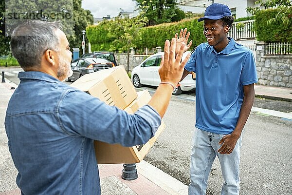 Reifer Mann  der mit einem afrikanischen jungen Mann High Five macht  nachdem er einige Pakete zu Hause erhalten hat