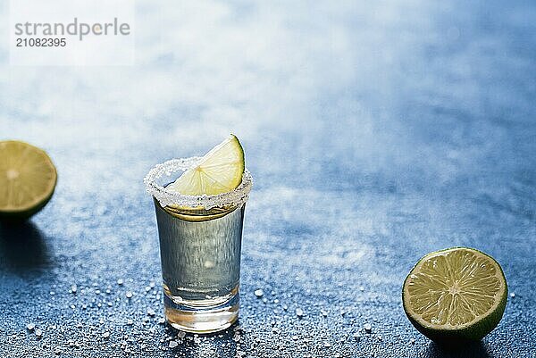 Tequila Shot mit Limettenscheibe und Salz auf einem blauen Tisch mit Hintergrundbeleuchtung. Leckeres mexikanisches Getränk. Ein Glas Alkohol. Sommerparty Getränk