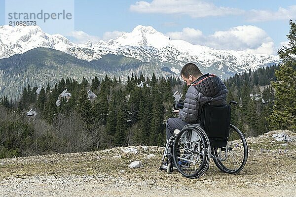 Foto eines Mannes im Rollstuhl mit Kamera in der Natur  der schöne Berge fotografiert