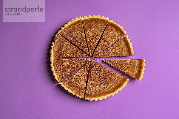 Ansicht eines in Scheiben geschnittenen Kürbiskuchens von oben  wobei ein Stück abgetrennt ist  auf einem lila Hintergrund. Minimalistische Lebensmittel Bild. Thanksgiving traditionelles Dessert