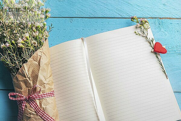 Aufgeschlagene Notizbuchseiten mit winzigem weißen Blumenstrauß und herzförmiger Holzklammer  auf blauem Hintergrund. Hochzeitsplanung Kontext. Frauen Tag Rahmen