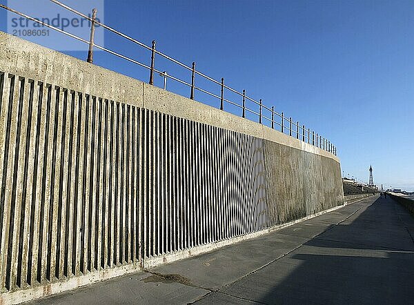 Concrete seawall and railings along the pedestrian promenade in north blackpool with the tower and town in the distance in afternoon sunshine