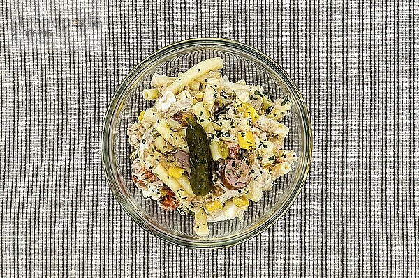 Nudelsalat mit Mais  Thunfisch und einer Gurke auf grauem Hintergrund