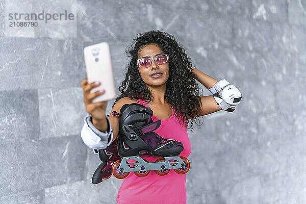 Selbstbewusste lateinische Frau  die ein Selfie mit Inline Skates im Freien auf einem städtischen Platz macht