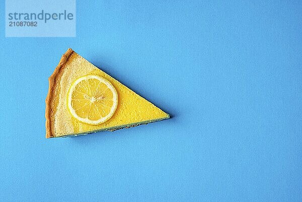 Scheibe gelber Zitronenkuchen  verziert mit einer Zitronenscheibe  auf blauem Hintergrund. Ansicht direkt von oben. Minimalistischer Stil. Leckeres Fruchtdessert