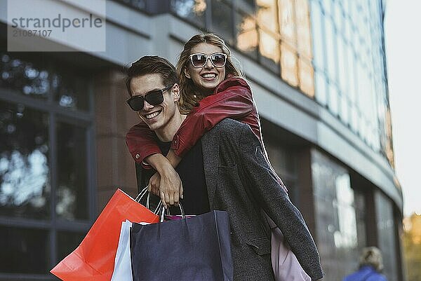 Happy couple shopping together and having fun. Boyfriend carrying his girlfriend on the piggyback