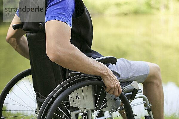 Glücklicher junger behinderter Mann in einem Rollstuhl sitzend in der Natur