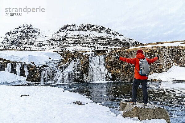 Ein Mann  der dem Kirkjufell Wasserfall im Winter in Island den Rücken zuwendet