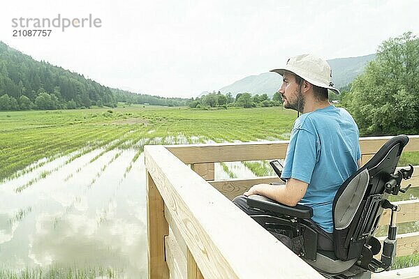 Photo of disabled Young man in electric wheelchair on a boardwalk enjoying his freedom and observing nature