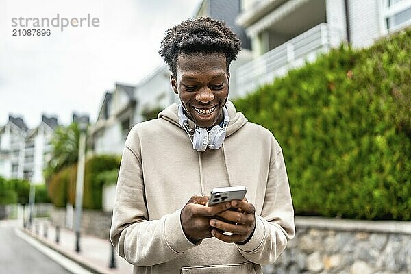 Selbstbewusster afrikanischer junger Mann  der lächelt und telefoniert  während er in einer Wohnstraße steht