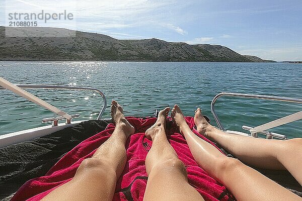 Blick auf Mann und Frau Beine liegen auf Yacht mit türkisblauem Meer und Strand mit grünen Palmen auf dem Hintergrund. Heterosexuelles Paar in Luxus Sommerurlaub Konzept