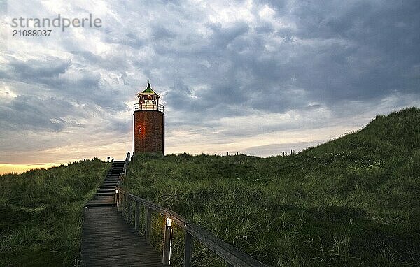 Sonnenuntergangslandschaft auf der Insel Sylt in der Nordsee  Deutschland. Schöne Landschaft mit roten Ziegeln Leuchtturm auf einer Anhöhe unter einem bewölkten Himmel