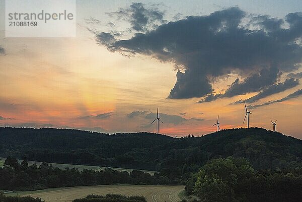 Schöner Sonnenaufgang Landschaft mit bewaldeten Hügeln  Wiesen und modernen Windkraftanlagen am Horizont  unter einem bunten Himmel  in der Nähe von Gaildorf Stadt  Deutschland  Europa