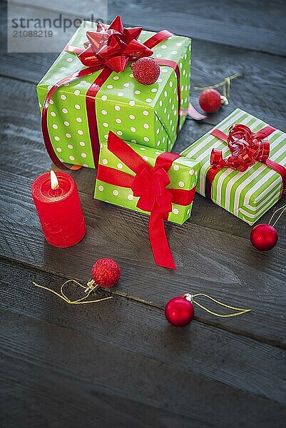 Viele fröhliche Geschenke  in grünes Papier eingewickelt und mit roten Bändern und Schleifen gebunden  umgeben von Weihnachtsschmuck und einer brennenden Kerze  auf einem alten Holztisch