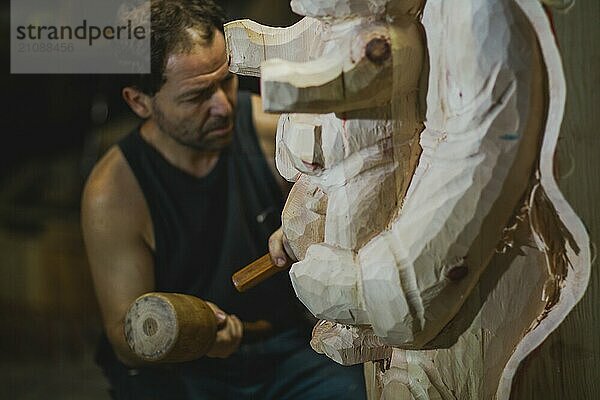 Ein Mann schnitzt in einer Werkstatt fleißig ein Stück Holz mit einem Hammer