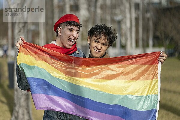 Junges homosexuelles Paar in einem Park  das eine Regenbogenflagge hält