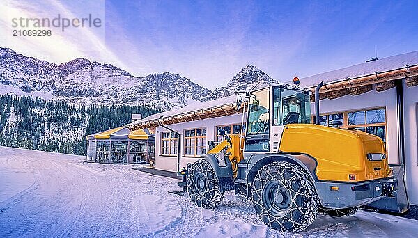 Ein gelber Radlader mit Ketten auf den Reifen  bereit  den Schnee von den Bergpfaden zu entfernen. Eine schöne Winterlandschaft in den österreichischen Alpen