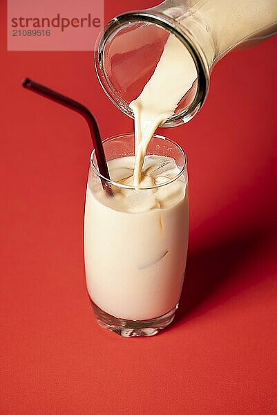 Einschenken von Horchata  mexikanischer Mandel und Reismilch in einem Glas mit Eiswürfeln auf rotem Hintergrund. Servieren eines kalten spanischen alkoholfreien Cocktails