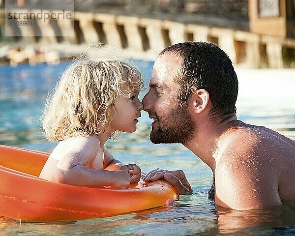 Glückliches Kind spielt mit Vater im blauen Wasser des Swimmingpools in einem tropischen Resort am Meer. Sommerferien Konzept