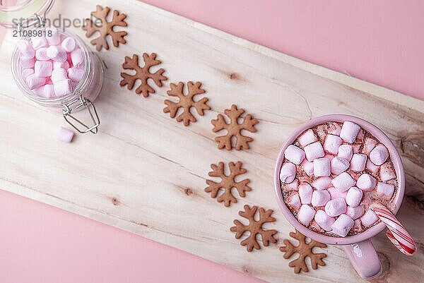 Amerikanische Wintersüßigkeiten  eine Tasse heiße Schokolade mit Mini Marshmallows  eine Zuckerstange und Lebkuchen in Form von Schneeflocken  auf einem Holztablett