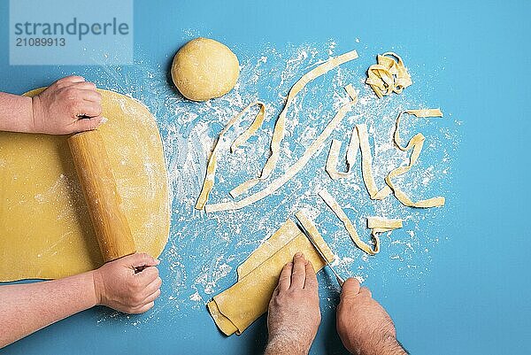 Paar bereitet italienische Pasta mit der Hand auf einem blauen Hintergrund. Flat Lay mit der Herstellung von Nudeln. Rolling Grieß gelben Teig. Formen von Tagliatelle Nudeln