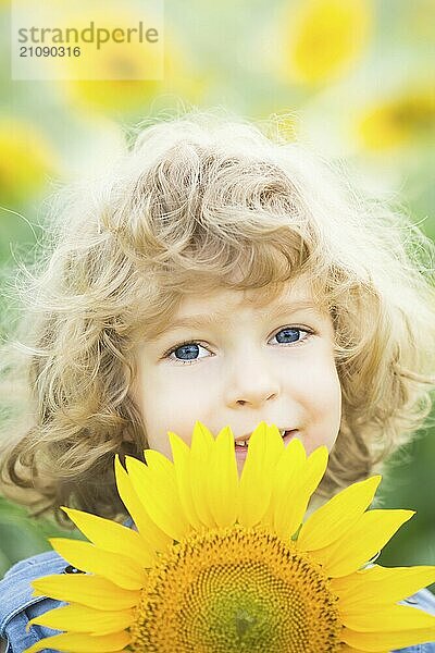 Glückliches lächelndes Kind mit Sonnenblume im Frühlingsfeld