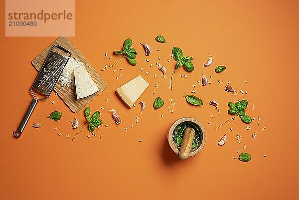 Herstellung von Pesto Sauce mit frischem Basilikum  Parmesan  Knoblauch und Pinienkernen in einem Mörser mit Stößel  auf orangefarbenem Hintergrund. Die Zubereitung von Pesto