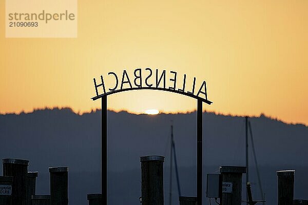 Ruhiger Sonnenuntergang mit einem farbigen Himmel und einer Silhouette eines Schriftzugs und Stegen im Vordergrund  Allensbach  Bodensee  Baden-Württemberg  Deutschland  Europa