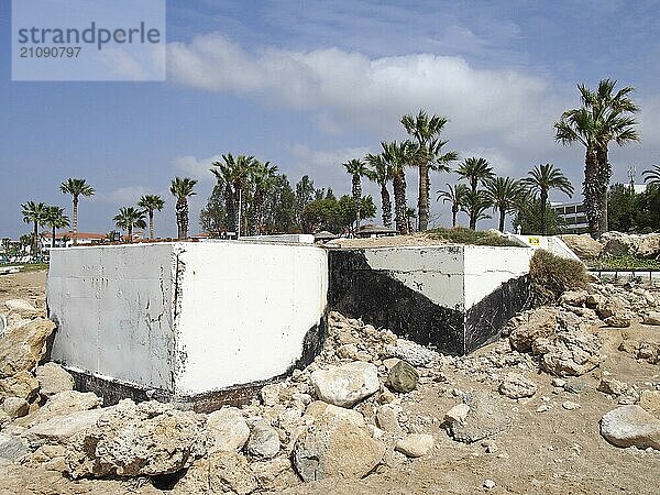 Verlassene weiß gestrichene Betonbunker aus der Zeit des Bürgerkriegs in Paphos  Zypern  mit Felsen am Strand neben Palmen und Hotels  Europa