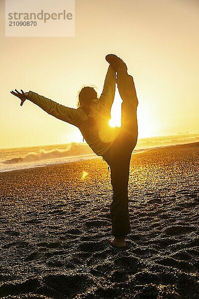 Eine Frau macht eine Yoga Pose an einem Strand bei Sonnenuntergang. Konzept der Entspannung und Ruhe  wie die Frau streckt ihren Körper in der warmen  goldenen Licht der untergehenden Sonne