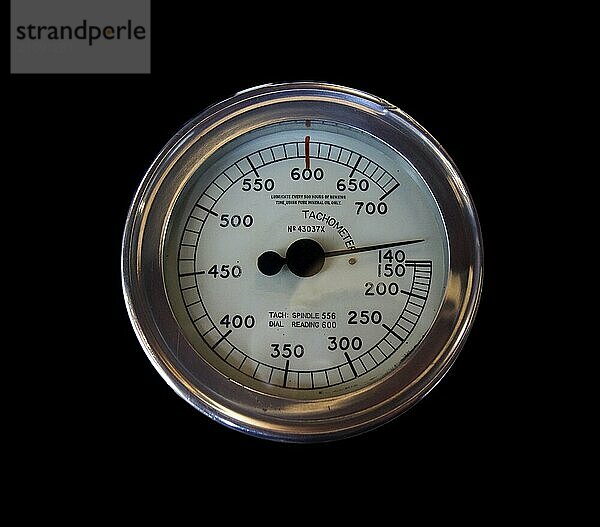 Ein alter runder Industrietachometer aus Metall auf schwarzem Hintergrund mit Zahlen auf einem weißen Zifferblatt