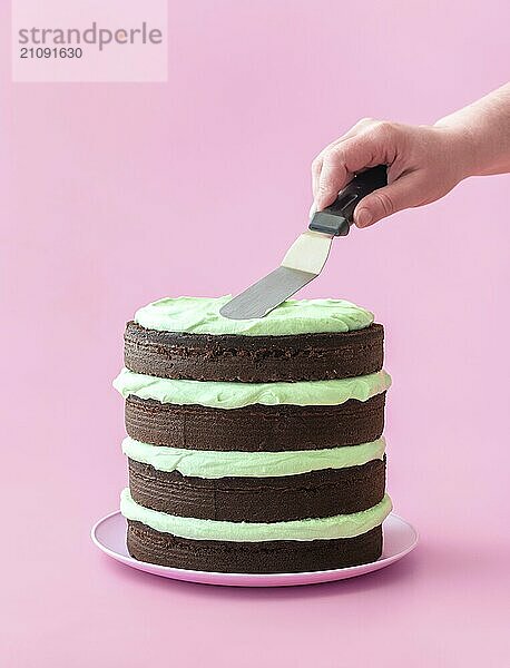 Frau macht einen Minz Schokoladenkuchen  minimalistisch auf einem rosa Hintergrund. Köstliche hausgemachte Schichtkuchen  mit dunkler Schokolade und Minze Aroma Buttercreme