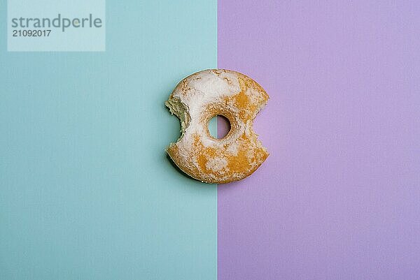 Leckerer Donut  gebissen von zwei Seiten  auf einem blauen und violetten Hintergrund. Flat lay image