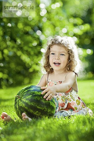 Glückliches Kind spielt mit Wassermelone gegen grünen Frühling Hintergrund