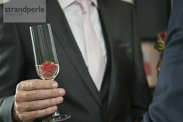 Mann im Anzug mit einem Glas Sekt oder Champagner und einer Erdbeere während eines Festes oder einer Feier wie einer Hochzeit  einem Geburtstag oder einem Neujahrstag