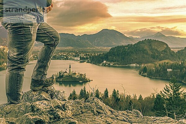 Bild mit den Beinen eines Touristen Mann kletterte auf Felsen über dem See Bled in Slowenien  Blick auf den schönen Sonnenaufgang und die Julischen Alpen