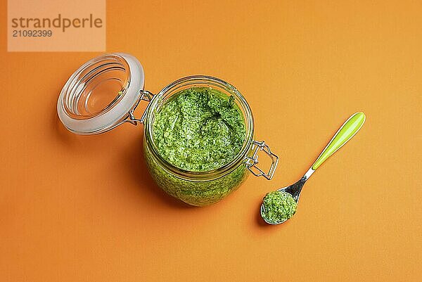 Geöffnetes Glas voller grüner Pesto Sauce auf einem nahtlosen orangefarbenen Hintergrund. Hausgemachtes Pesto aus Basilikum  Käse  Knoblauch und Öl. Italienische Nudelsauce