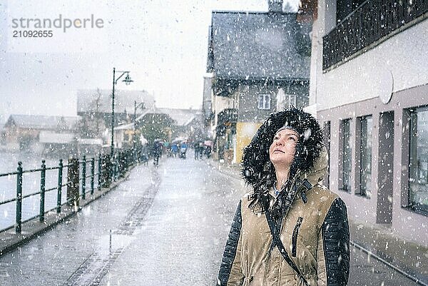 Fröhliche Winterzeit mit einem schönen Mädchen  das den Schneefall genießt und in den Himmel schaut  in den Straßen von Hallstatt  einer der Welterbestätten in Österreich