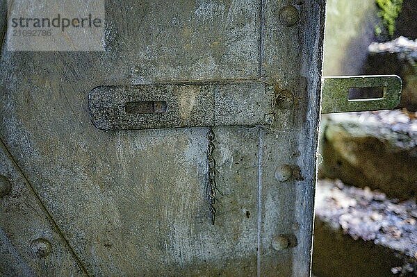 Bunkertür Cheneux  2. Weltkrieg  gebaut 1933-1936  Ardennen Offensive  schwere Tür verwittert  an ihr hängt eine Metallkette vom ehemaligen Schloss  rechts die Treppenstufen nach draußen sichtbar  verschwommen  Cheneux  Ardennen  Belgien  Europa