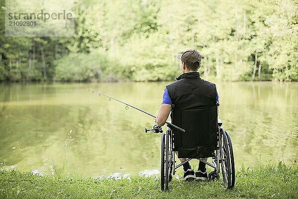 Fröhlicher und junger behinderter Mann beim Angeln an einem See in der Natur. Beliebter Sport für Querschnittsgelähmte